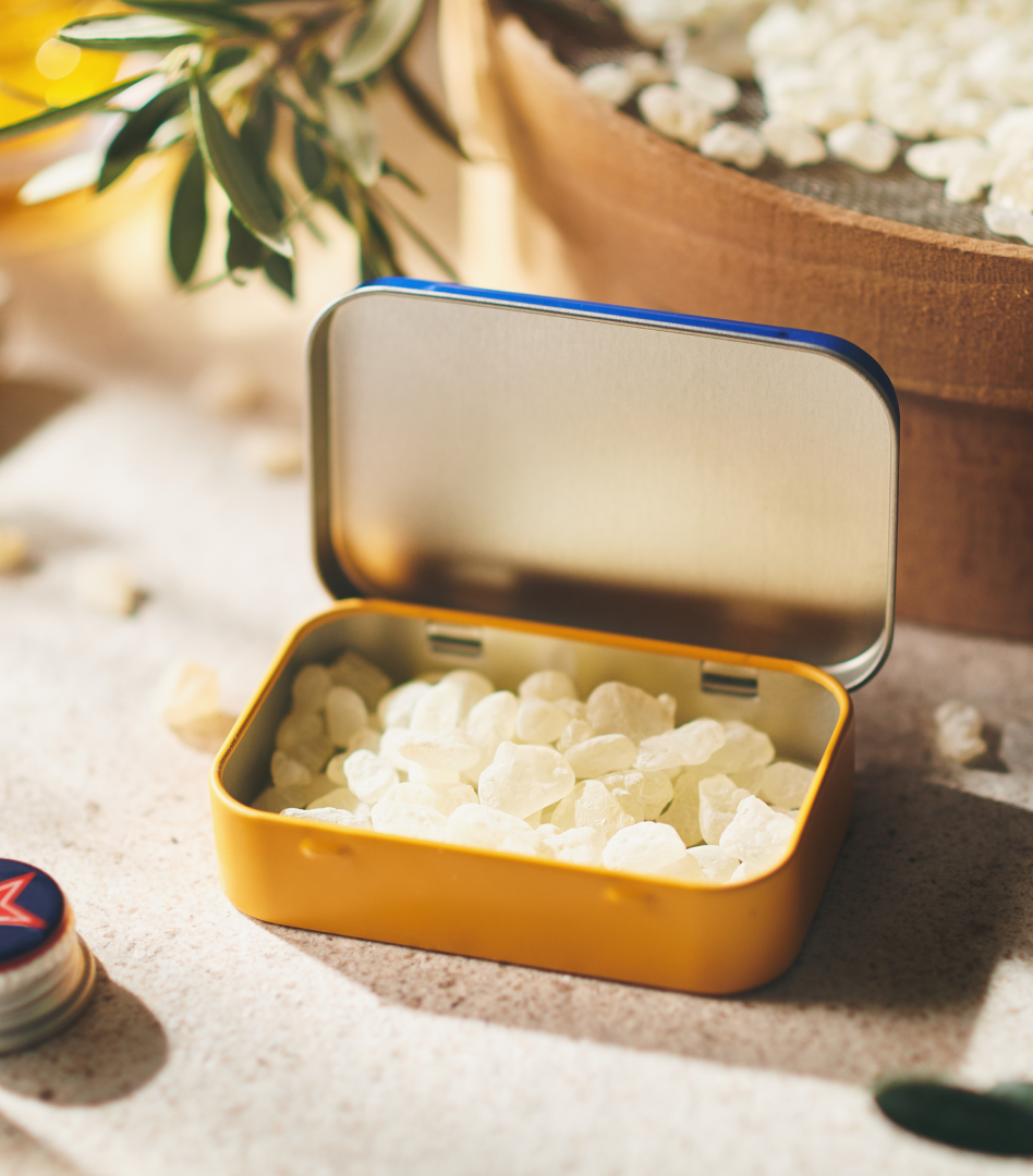 Blue and ochre Greco Gum tin with the lid open, revealing a thick layer of mastic gum