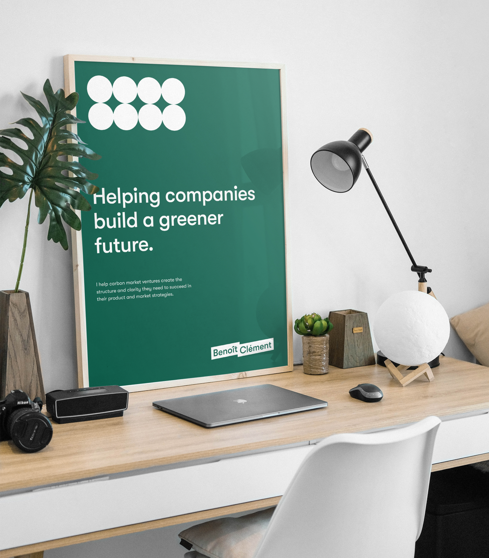 Framed poster standing on a desk. The poster bears Benoît's branding, with text that says "Helping companies build a greener future."