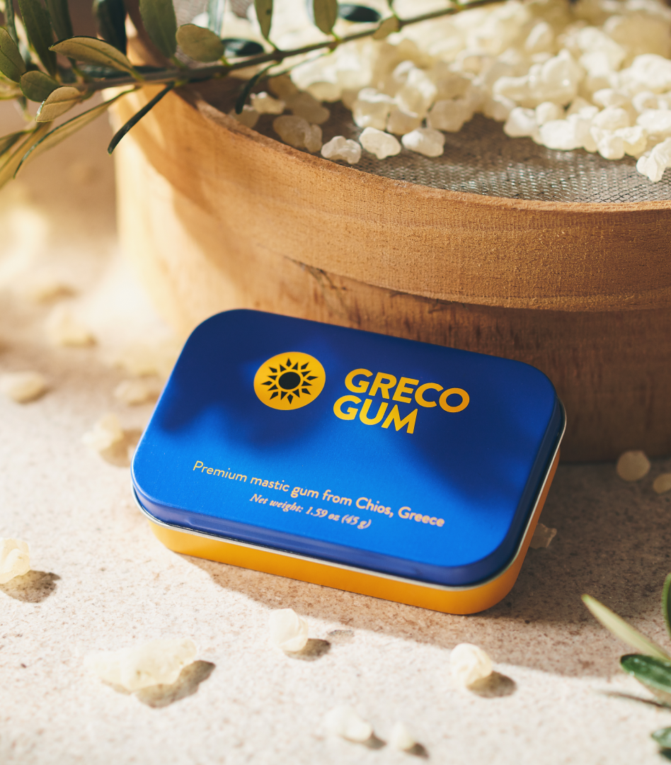 Packaging Greco Gum tin in blue and ochre, surrounded by mastic gum