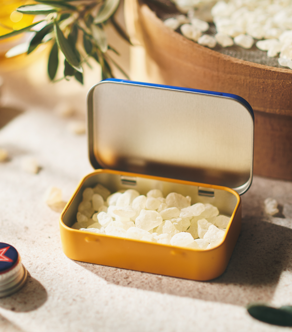 Packaging Blue and ochre Greco Gum tin with the lid open, revealing a thick layer of mastic gum